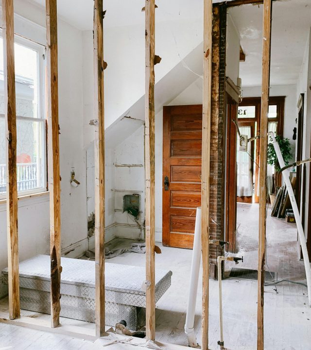 Interior view of a home under renovation with exposed wooden beams and door.